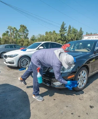 Fashion Square Car Wash detailer cleaning the front bumper of a black sedan in the parking lot